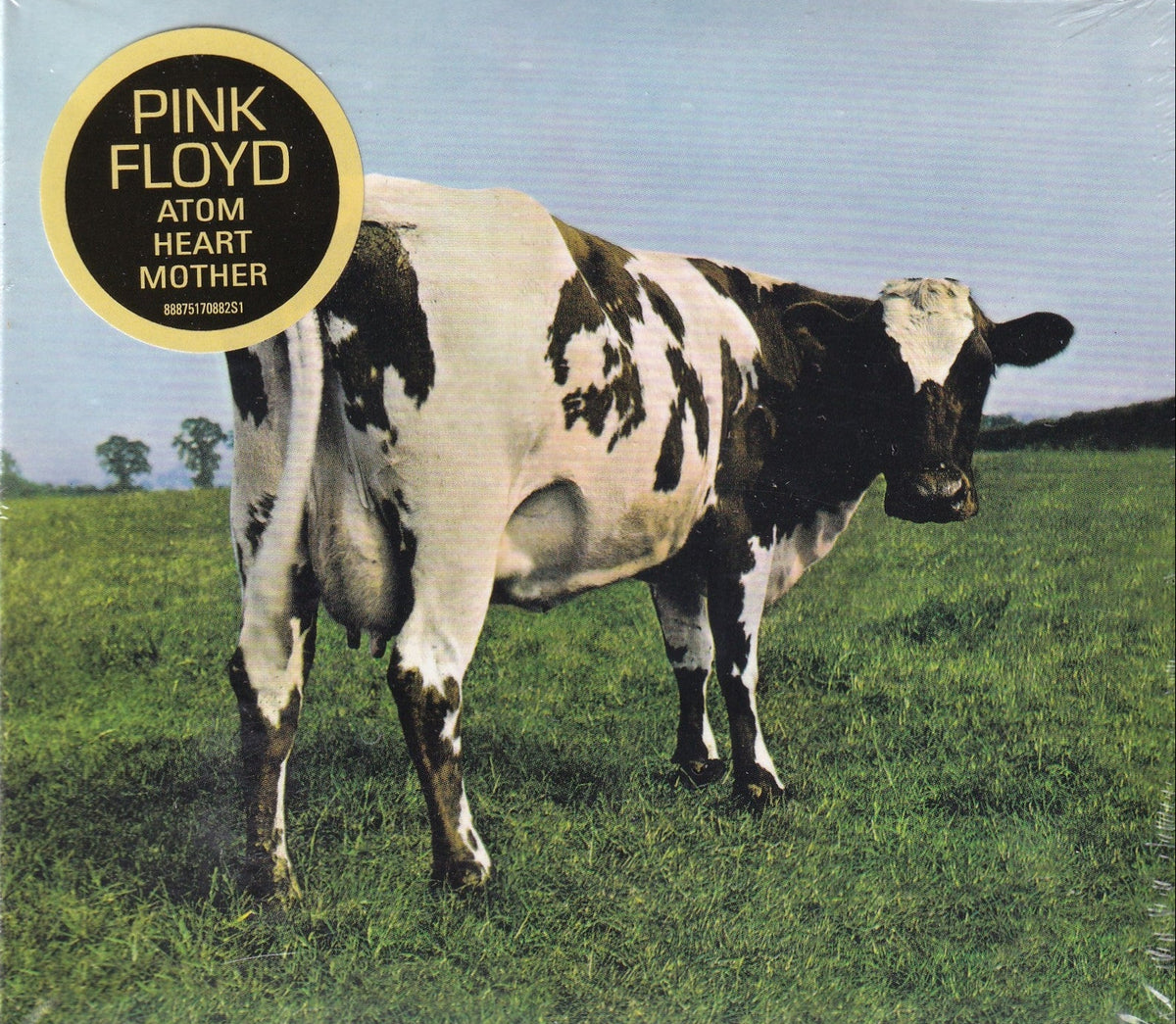 Pink Floyd 'Atom Heart Mother' vinyl record cover featuring a black and white cow standing in a green field under a pale blue sky, with a gold circular logo in the top left.